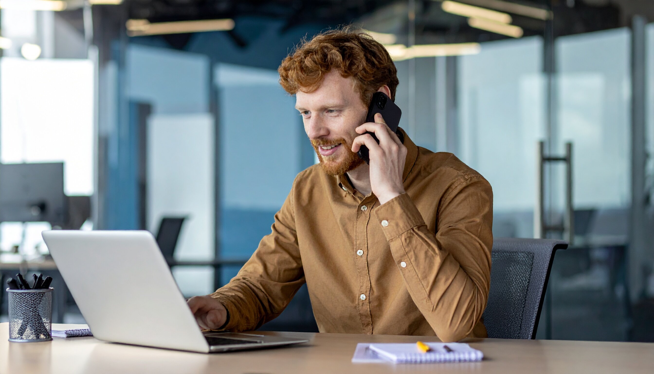 Mann telefoniert und arbeitet am Laptop im Büro.