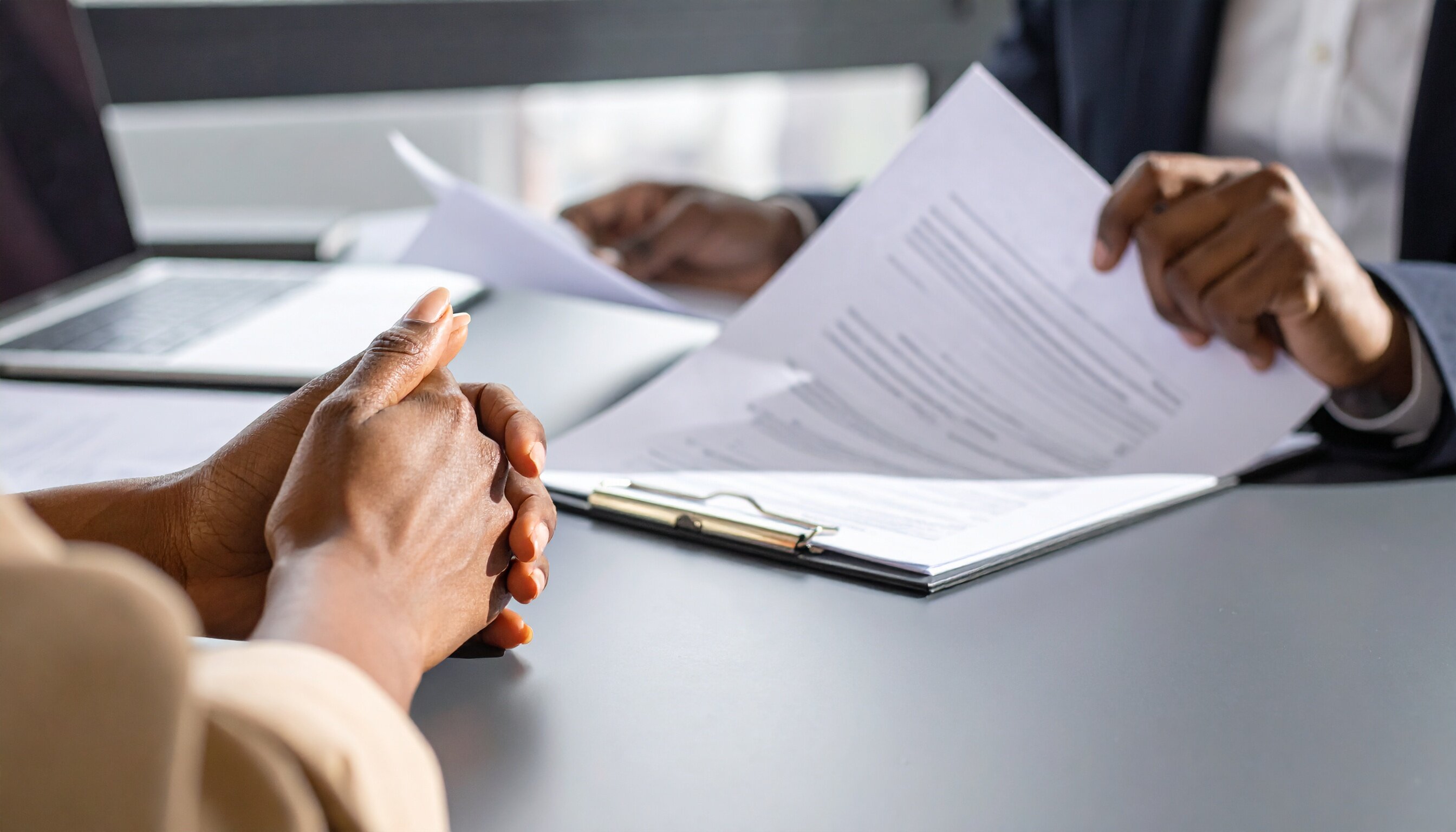 Eine Situation in einem Büro. Zwei Personen sitzen sich gegenüber, es sind keine Gesichter zu sehen. Eine Person blättert Zettel durch