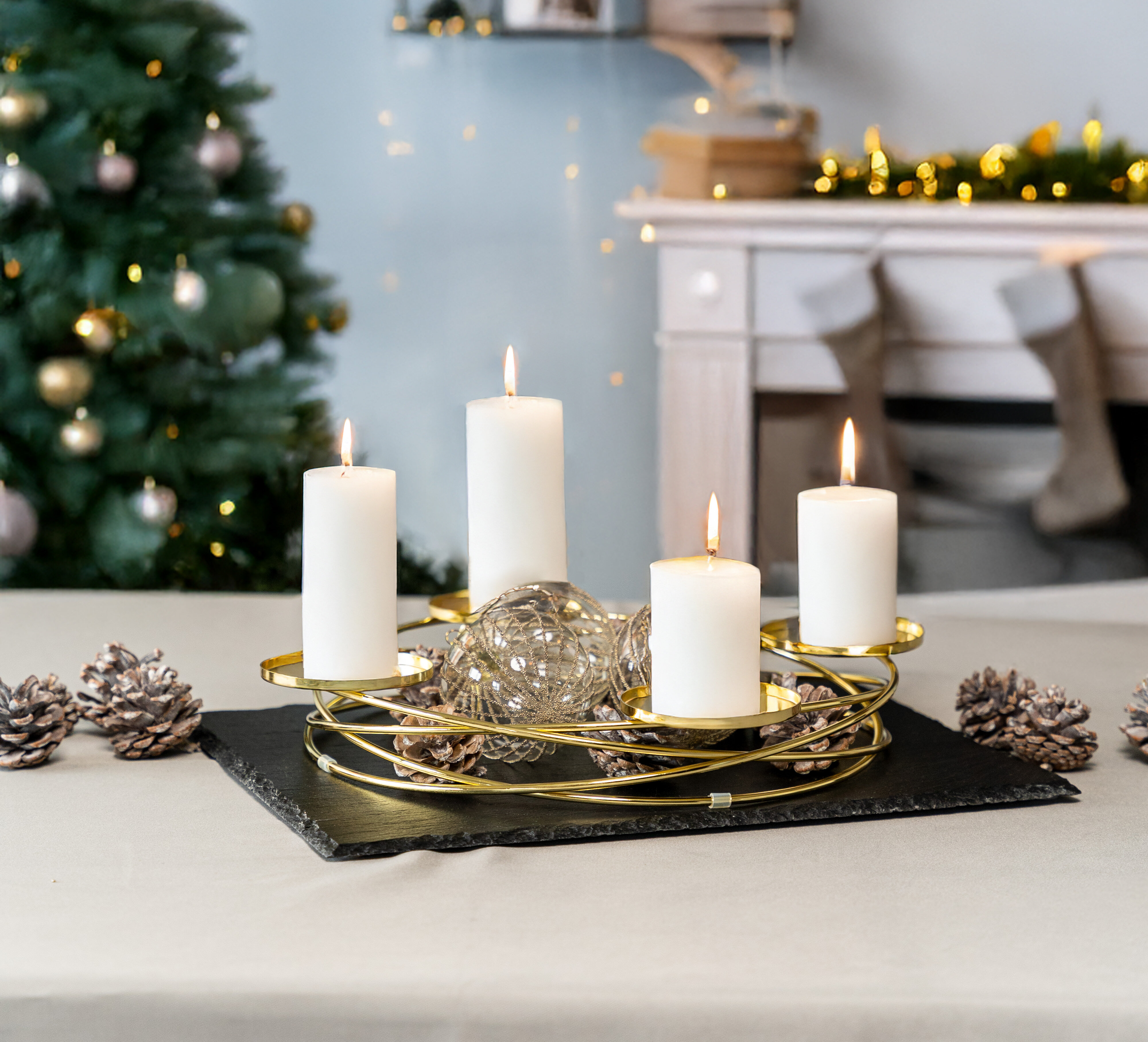 Vier weiße, brennende Kerzen stehen auf einem goldenen Kerzenhalter, umgeben von Tannenzapfen. Im Hintergrund ist ein Weihnachtsbaum sichtbar.