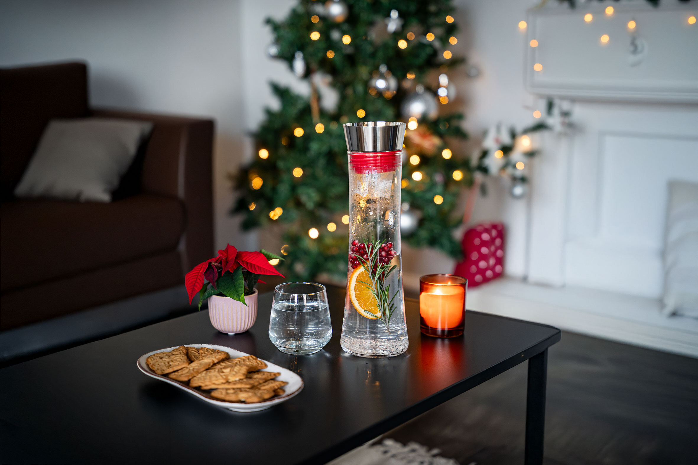 Weihnachtsdeko mit Wasserkaraffe, Orange und Rosmarin, Kerze, Lebkuchen und Poinsettie.