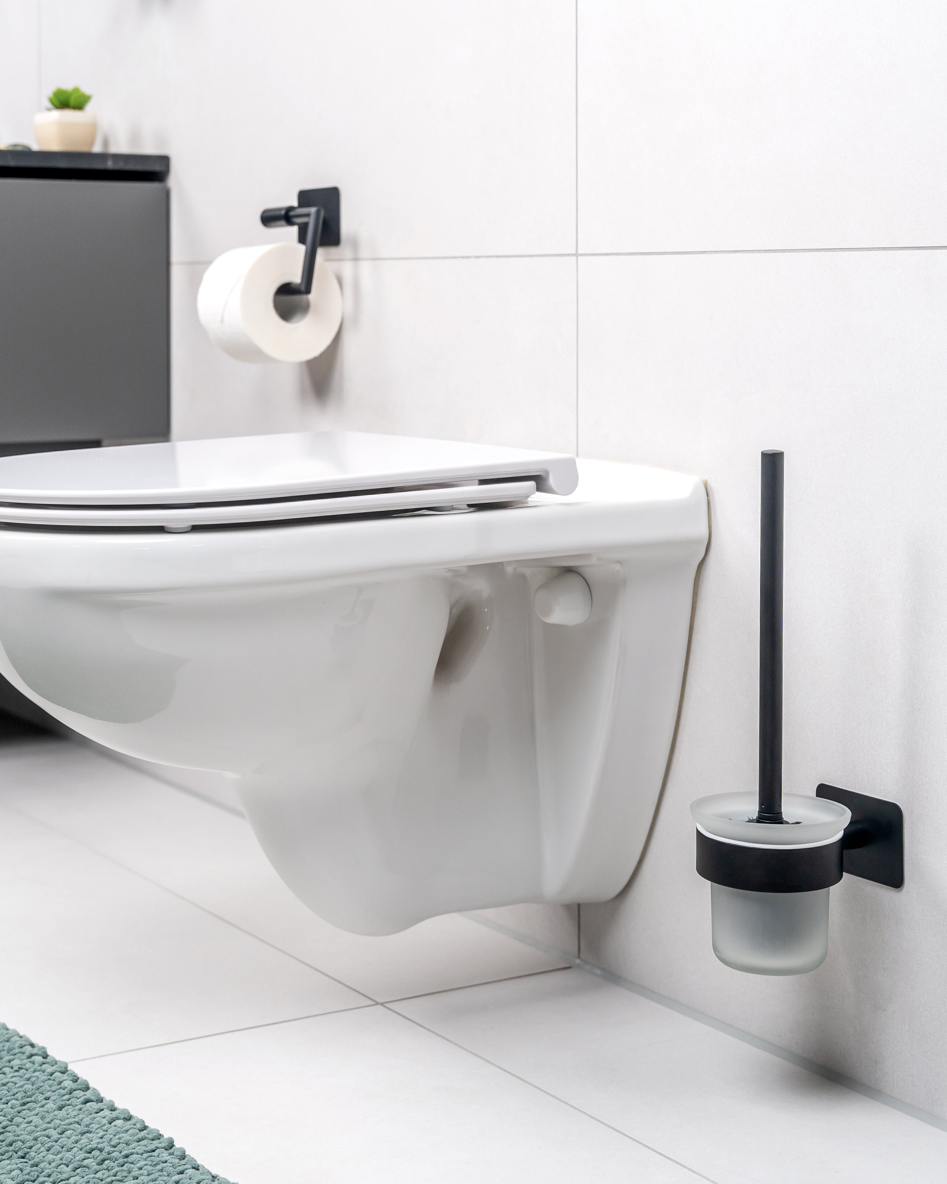 Modernes Badezimmer mit einer eleganten weißen Wandtoilette, einer schwarzen Toilettenbürste im Halter und einem minimalistischen Toilettenpapierhalter. Klares, zeitgemäßes Design.