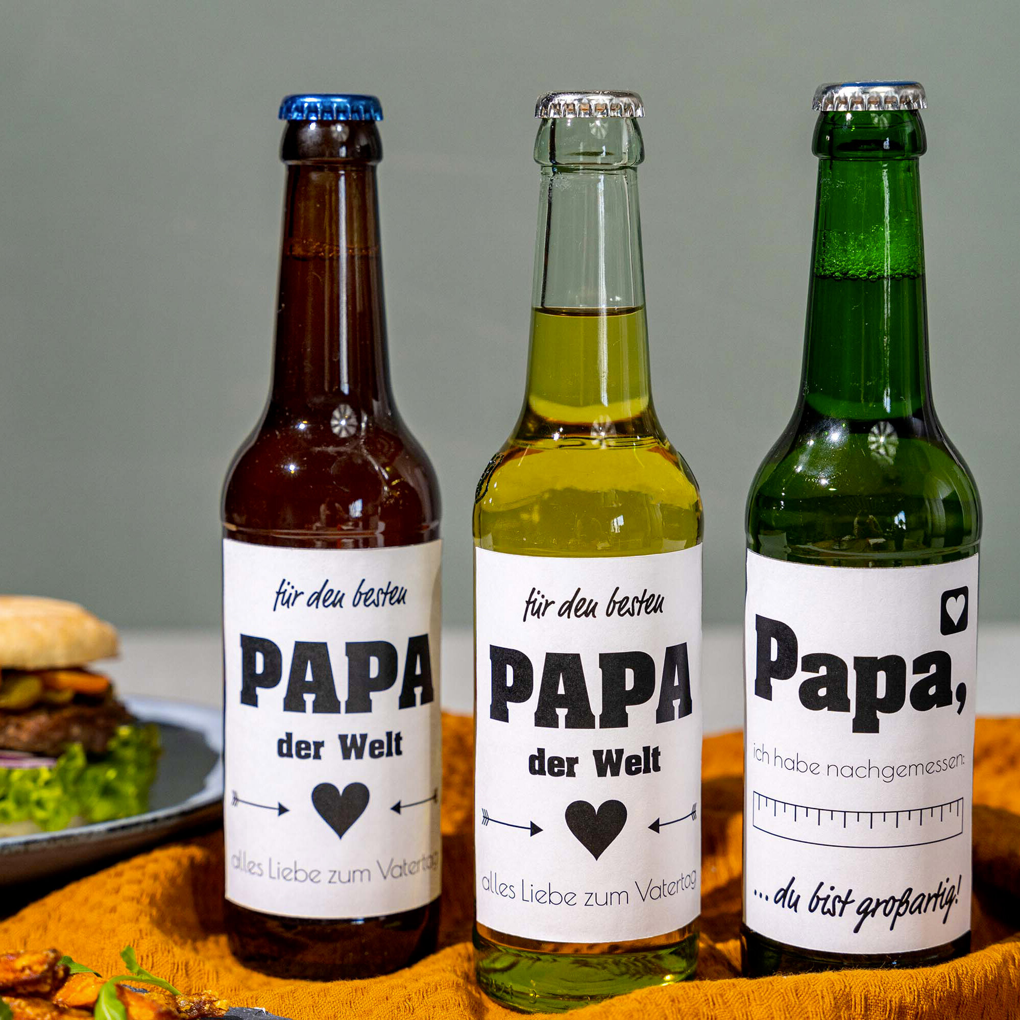 Drei Bierflaschen mit "Papa" Etiketten auf Tisch.