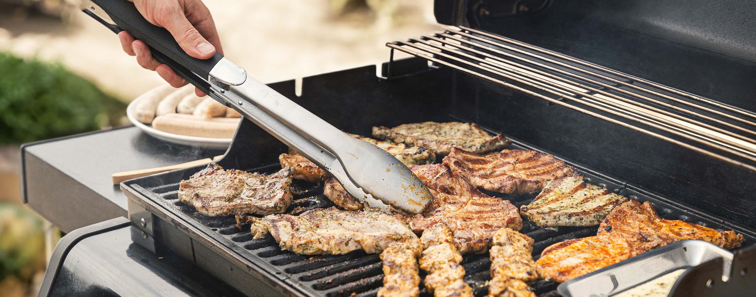 Eine Person bereitet Fleisch auf einem Grill vor und hält eine Grillzange