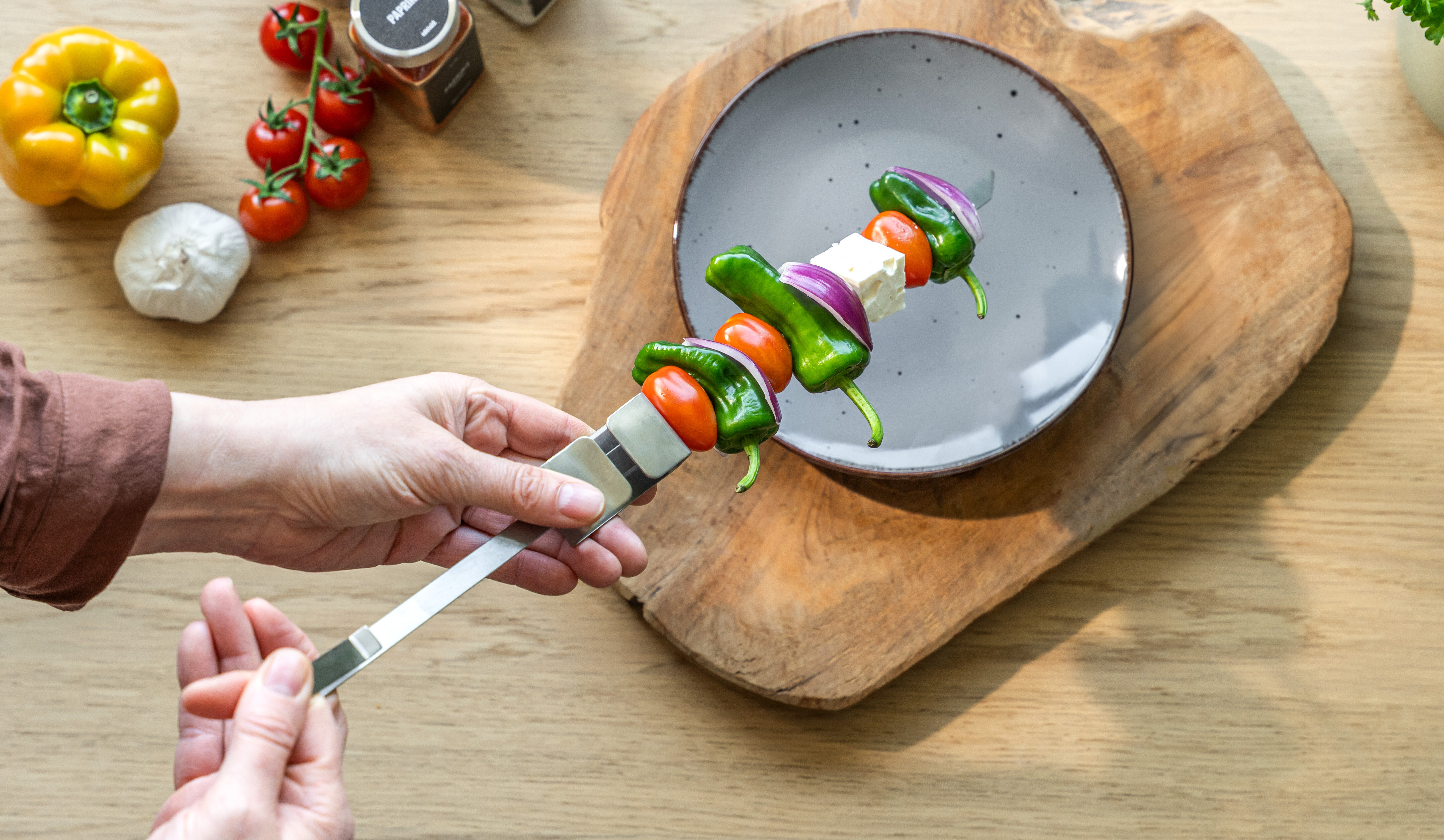 Eine Person hält einen Grillspieß mit frischem Gemüse über einem Teller. 