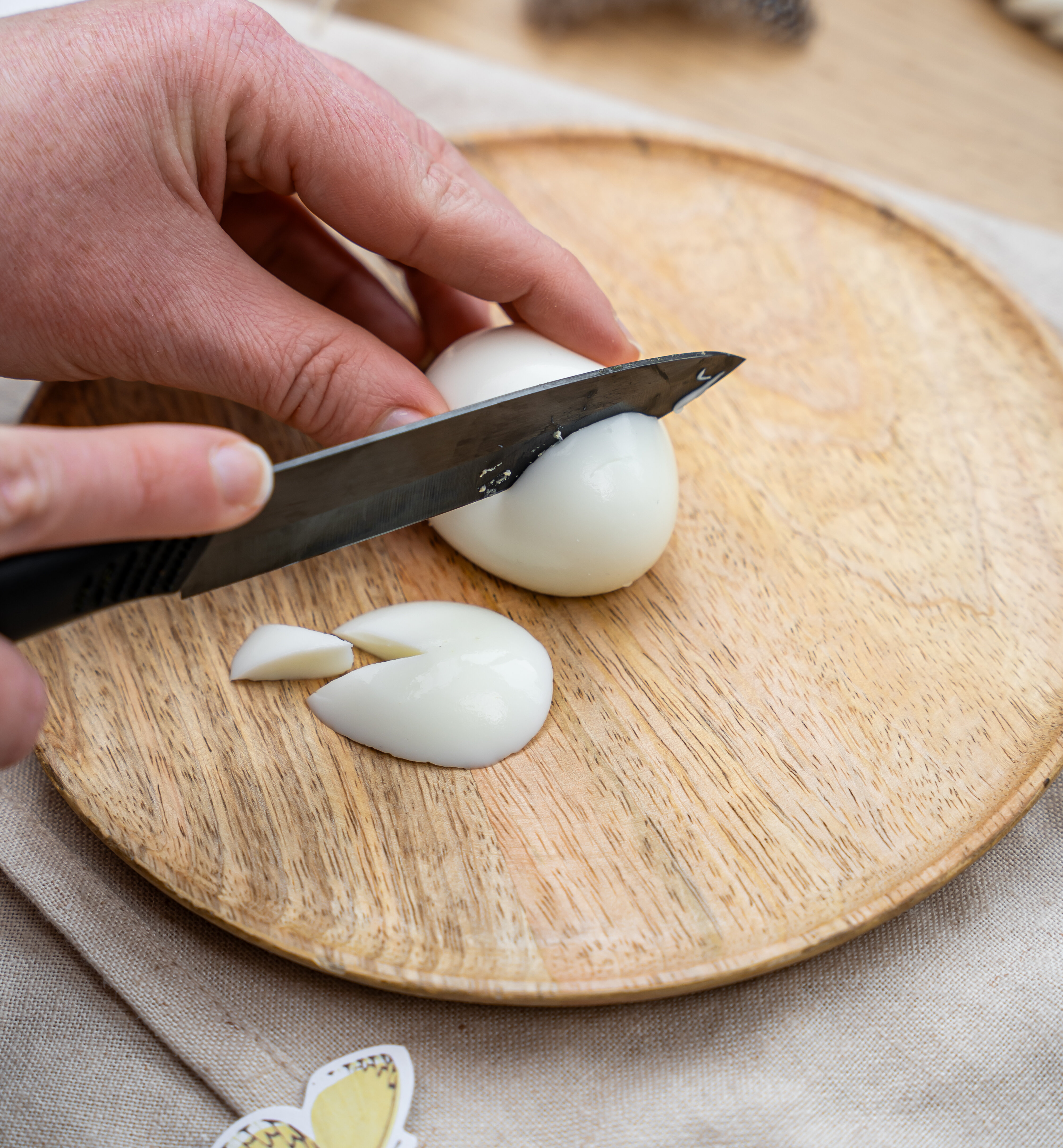 Hand schneidet weiße Zwiebel auf rundem Holzbrett mit schwarzem Messer