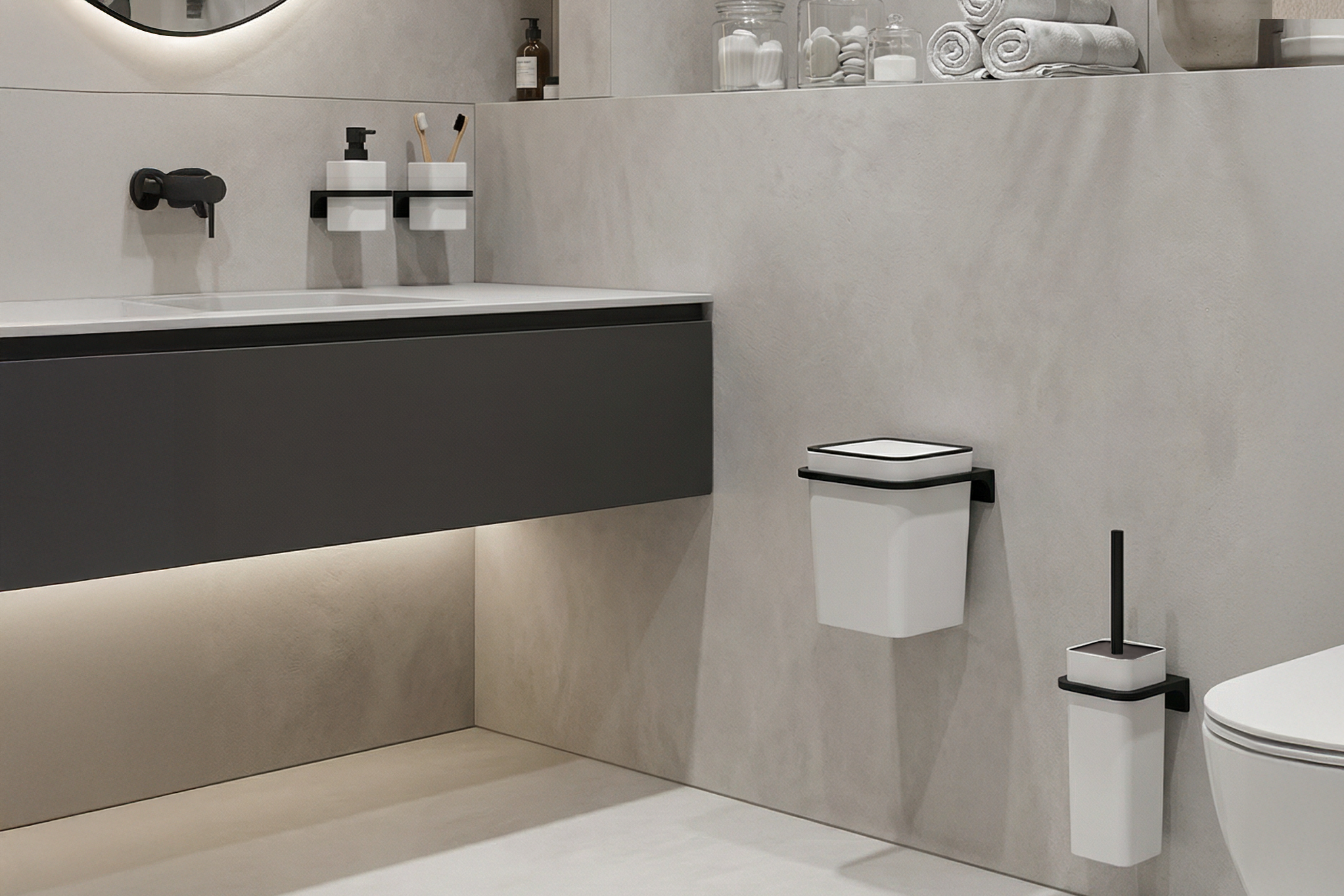 weiße, wandmontierte Badezimmer-Accessoires: ein Mülleimer mit Deckel und ein Toilettenbürstenhalter mit schwarzem Griff. Am Waschbecken sind Zahnputzbecher und Seifenspender montiert.