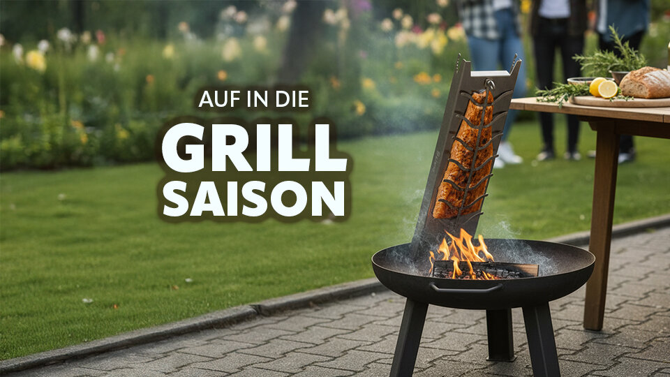 Mobiler Flammlachshalter mit brennendem Feuer und Lachsstücken vor einem Tisch im Garten mit Menschen im Hintergrund und dem Text 'AUF IN DIE GRILL SAISON'