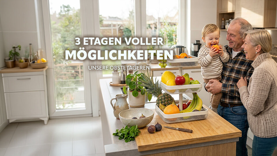 Dreistöckige Obstschale mit verschiedenen Früchten auf einer Küchenarbeitsplatte, im Hintergrund ein Mann hält ein Kleinkind