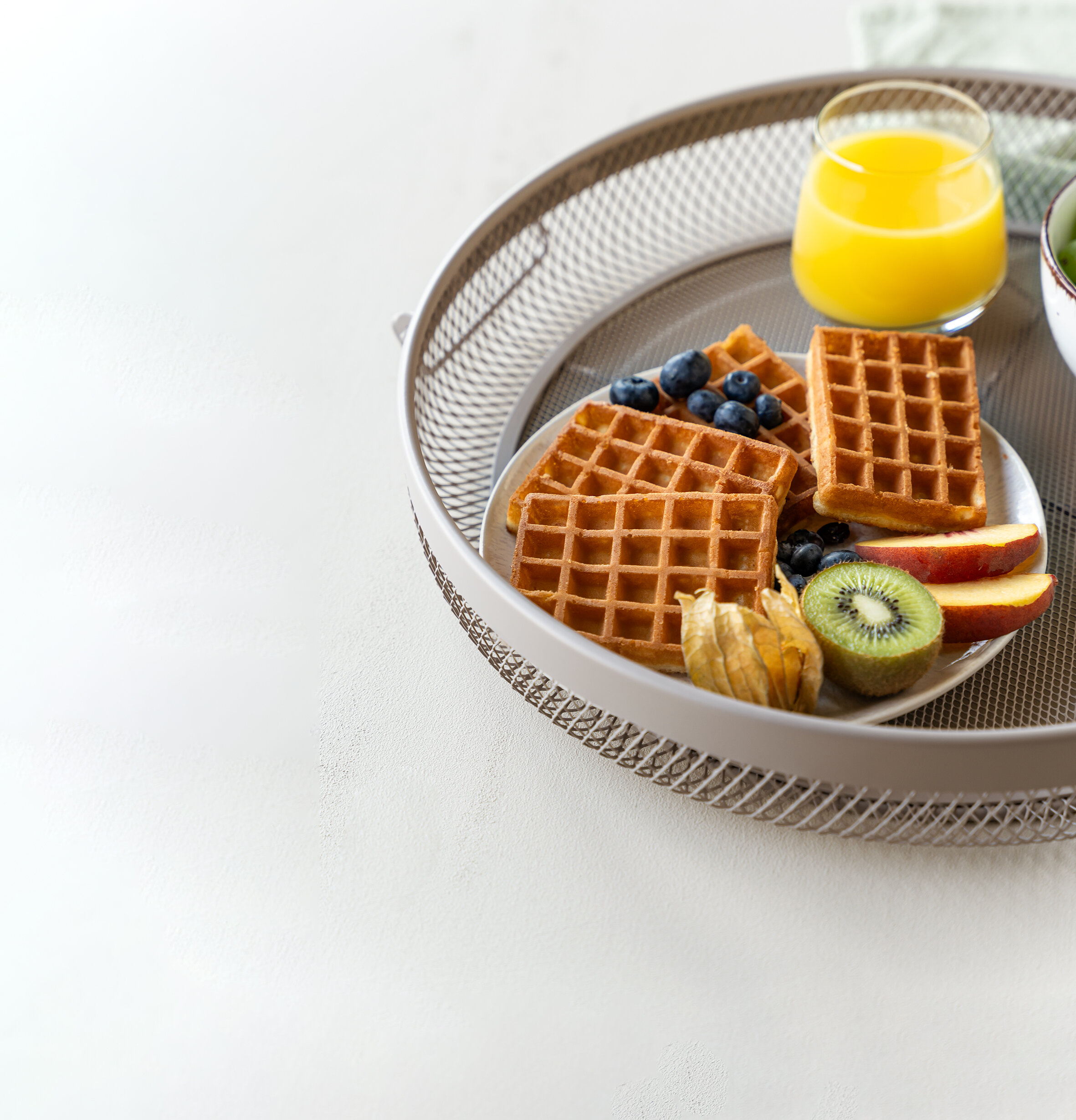 Rundes Serviertablett mit einem Teller Waffeln, Beeren, Kiwi und einem Glas Saft