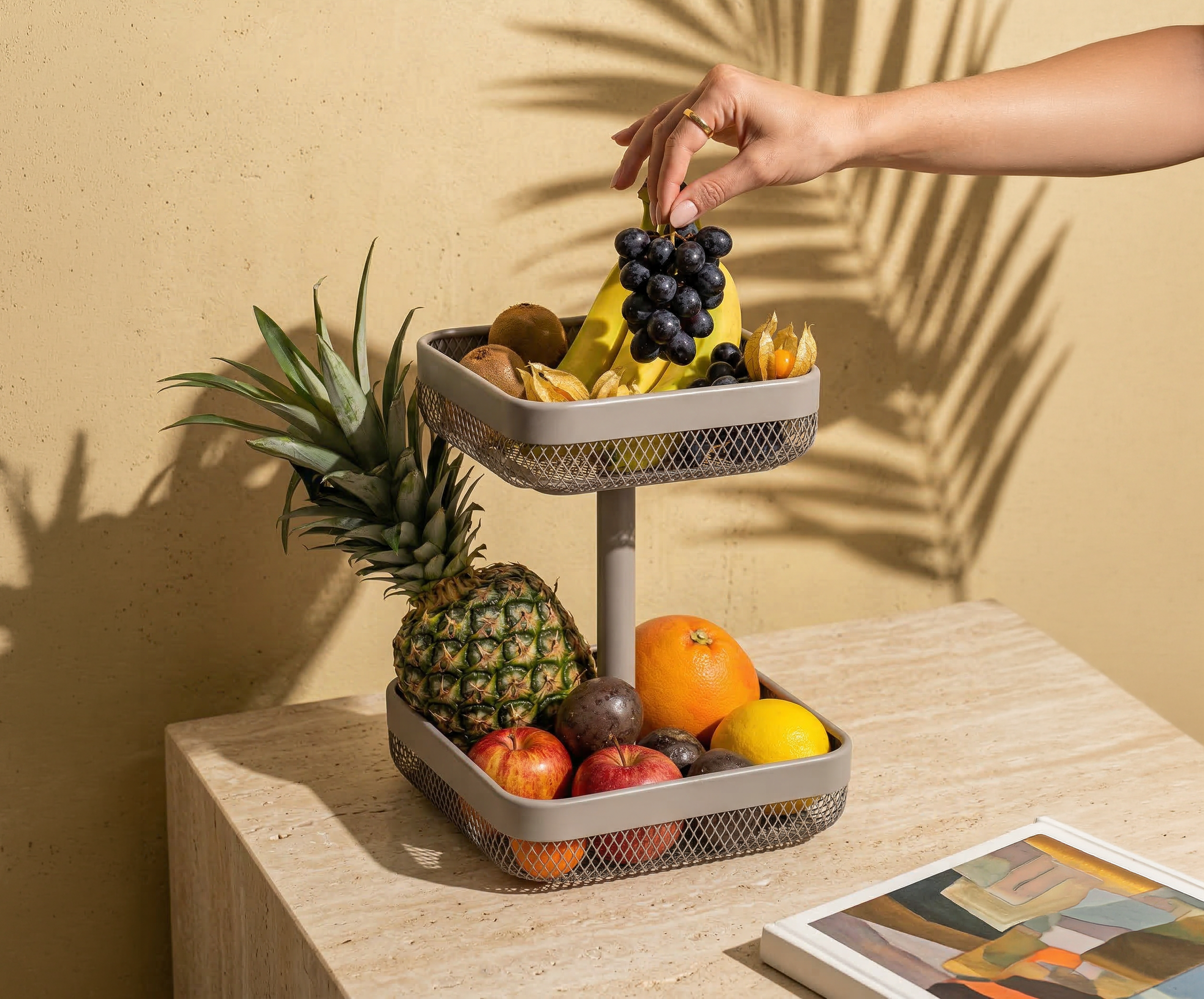 Zweistöckige eckige Obstetagere mit verschiedenen Früchten auf einem Tisch und einer Hand, die eine Traube hält