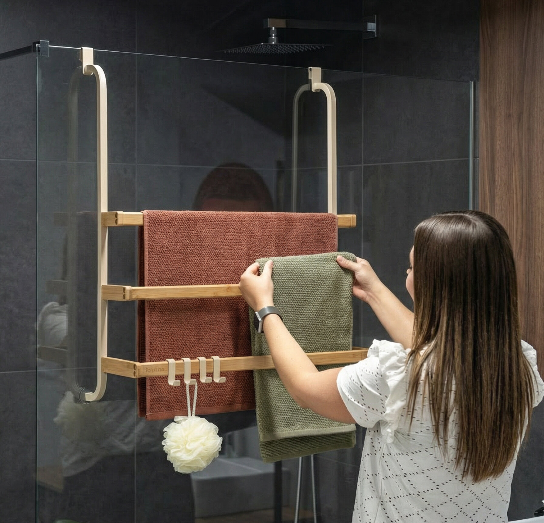 Frau hängt ein Handtuch an einen beigen Handtuchhalter aus Holz, der an einer Glasduschwand befestigt ist. KI-generiert